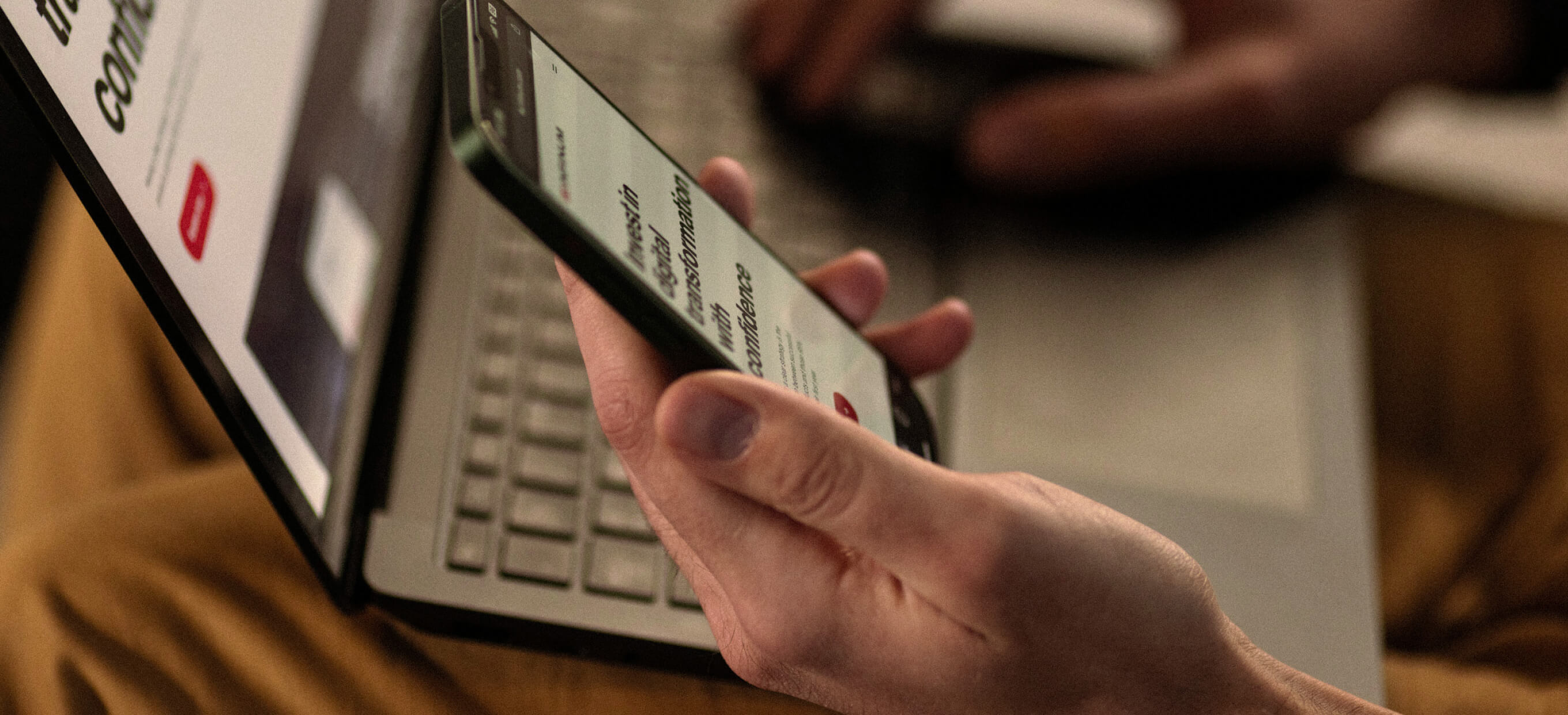 Person using a smartphone and laptop simultaneously, representing mobile and web app development solutions for seamless digital experiences.